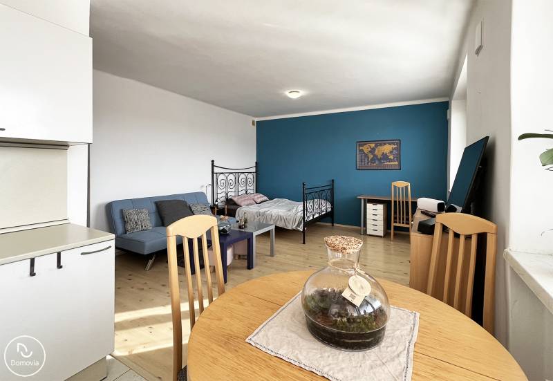 1 szobás lakás belső tere fa hatású padlóval, kanapéval és íróasztallal.