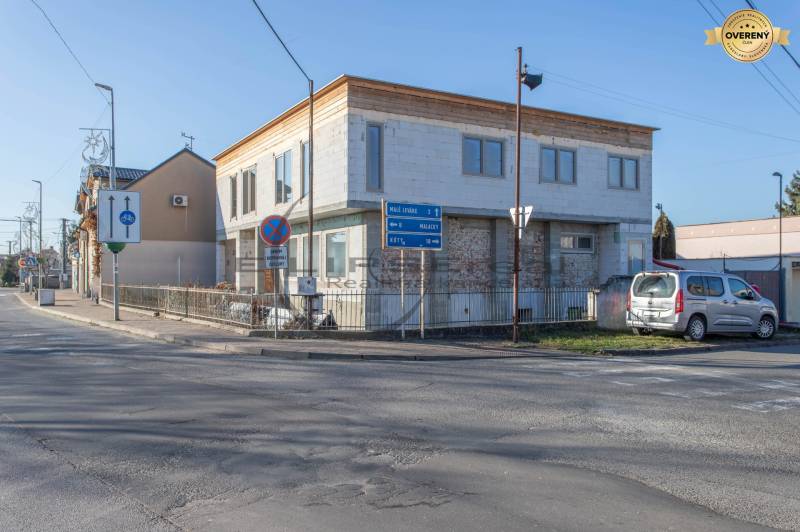 Épület Nagyléváron, az út mellett, parkoló autóval és közlekedési táblákkal.