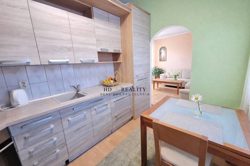 Konyhapult fa dekorral, padlóval és étkezőasztallal egy kétszobás lakásban.