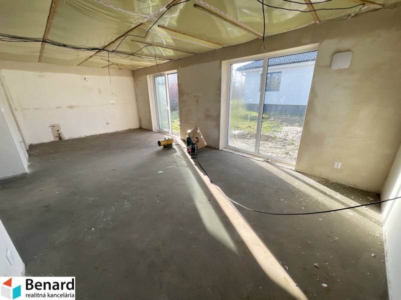 Üres szoba nagy ablakokkal egy családi házban, padlóburkolat nélkül.