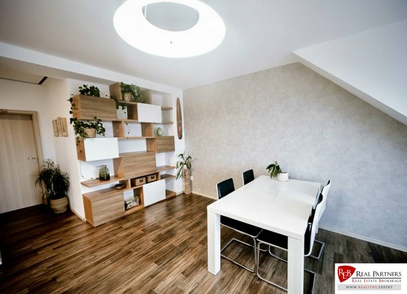 Étkezőasztal, székek és polcok dekorációs elemekkel egy háromszobás lakásban, fa dekoros padlóval.