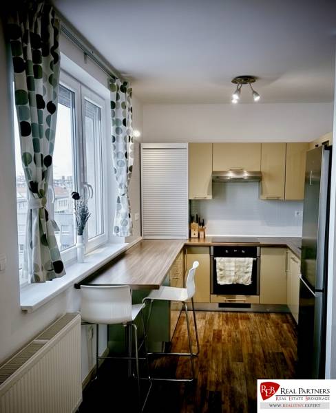 Konyha egy 3 szobás lakásban bárpulttal, fa hatású padlóval és nagy ablakkal.