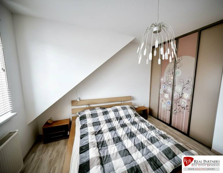 Hálószoba egy háromszobás lakásban ággyal, beépített szekrénnyel és fa dekorációjú padlóval.