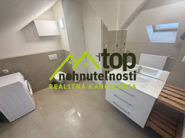 Tetőtéri egyszobás lakás fürdőszobája mosógéppel és mosdóval, fa dekor padlóval.