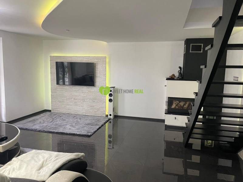 Nappali egy családi házban lépcsőházzal, kandallóval és falra szerelt televízióval.