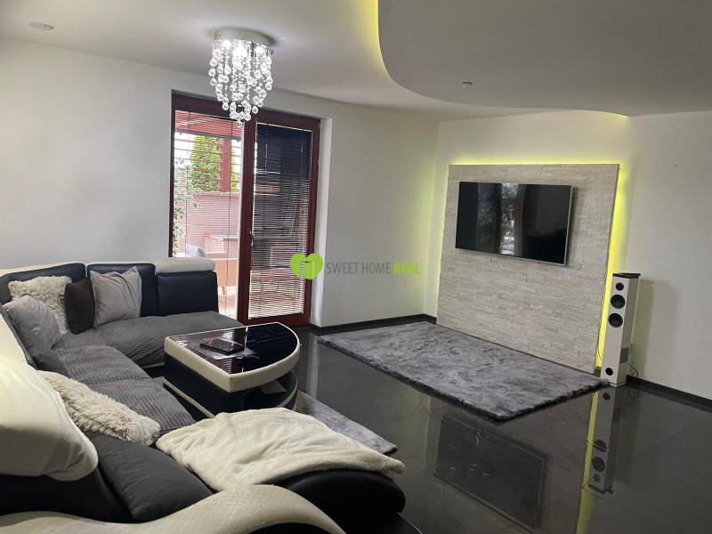 Nappali egy családi házban kanapéval és televízióval a kőburkolatú falon.