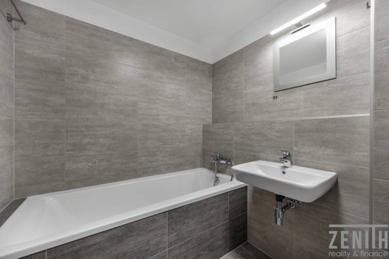 Fürdőszoba egy kétszobás lakásban káddal, mosdóval és szürke csempékkel.