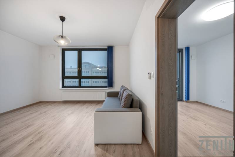 Nappali kanapéval, nagy ablakkal és fa dekorációjú padlóval egy kétszobás lakásban.