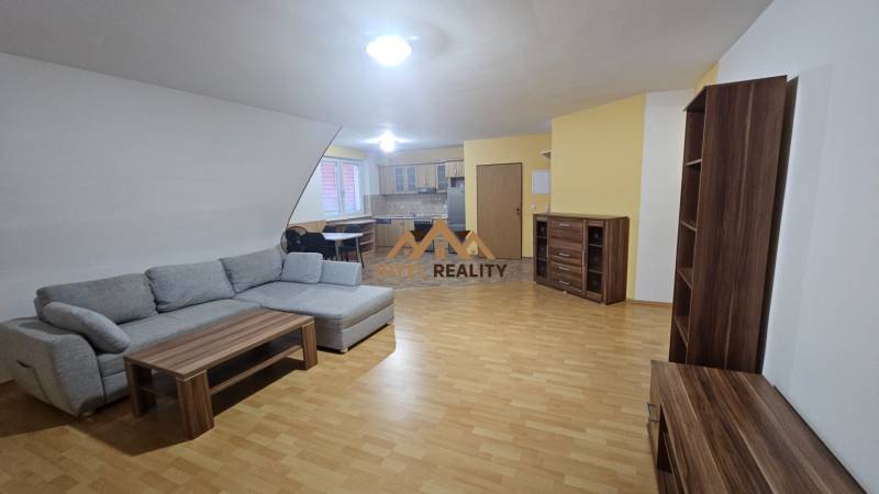 Nappali kanapéval, konyhával és fa dekorációjú padlóval egy háromszobás lakásban.