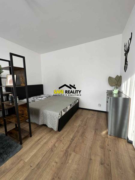 Hálószoba egy egyszobás lakásban, fa mintázatú padlóval és minimalista berendezéssel.