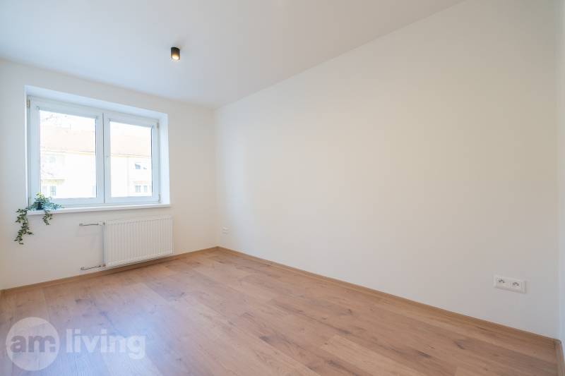 Világos szoba fa dekorációjú padlóval egy háromszobás lakásban, ablakkal szembeni lámpával.