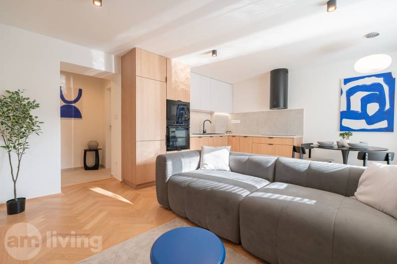 3 szobás lakás nappali része konyhával, szürke kanapéval és fa dekorációjú padlóval.