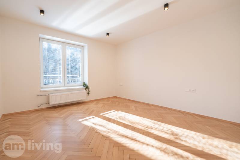 Világos szoba egy 3 szobás lakásban fa dekor padlóval és nagy ablakkal.