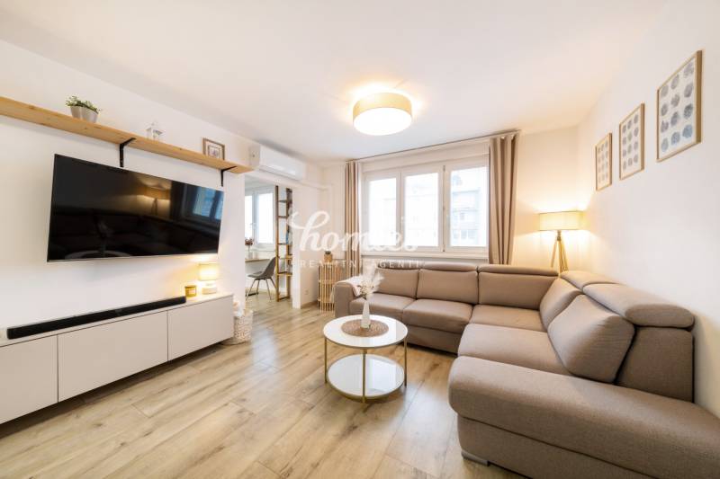 Nappali egy kétszobás lakásban kényelmes kanapéval és fa hatású padlóval.