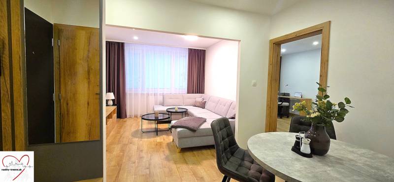 A háromszobás lakás nappalija kanapéval, asztallal és fa dekorációjú padlóval.