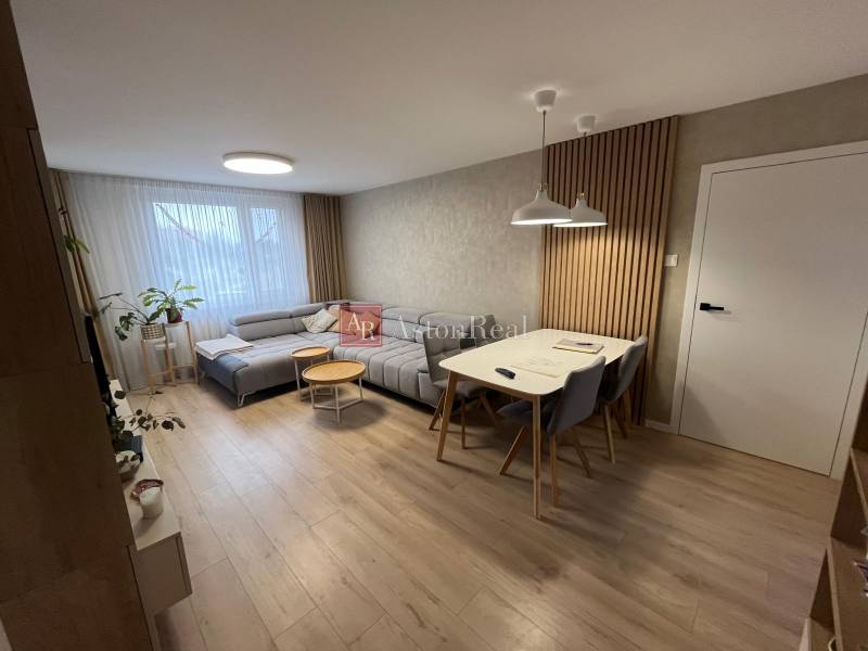 Nappali egy négy szobás lakásban, fa dekor padlóval, szürke kanapéval és étkezőasztallal.