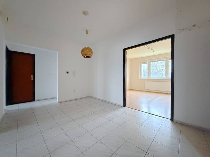 A csempézett folyosó egy világos nappaliba vezet, amelynek padlója fa dekorációval van ellátva.