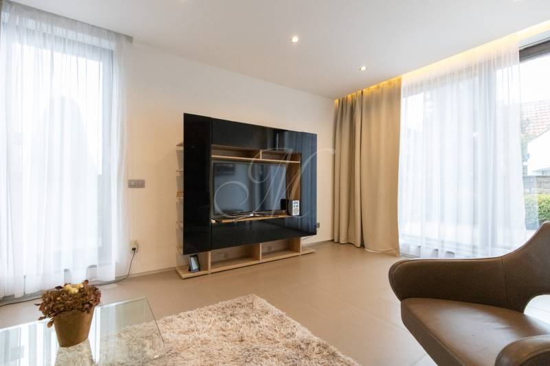 Nappali egy kétszobás lakásban világos függönyökkel és televíziós fallal.