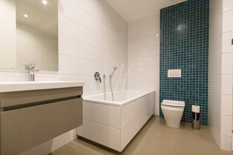 Fürdőszoba egy kétszobás lakásban káddal, mosdóval és zöld csempés panellel.