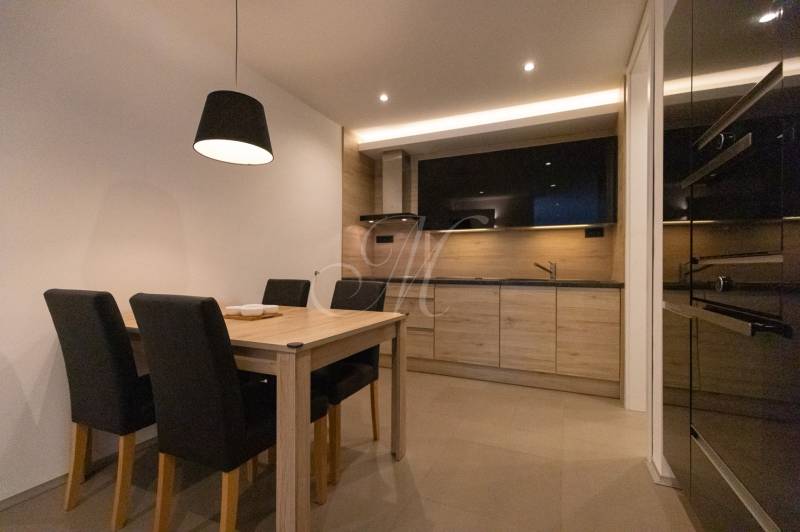 Konyha egy kétszobás lakásban, fa dekorációval, étkezőasztallal és fekete székekkel.