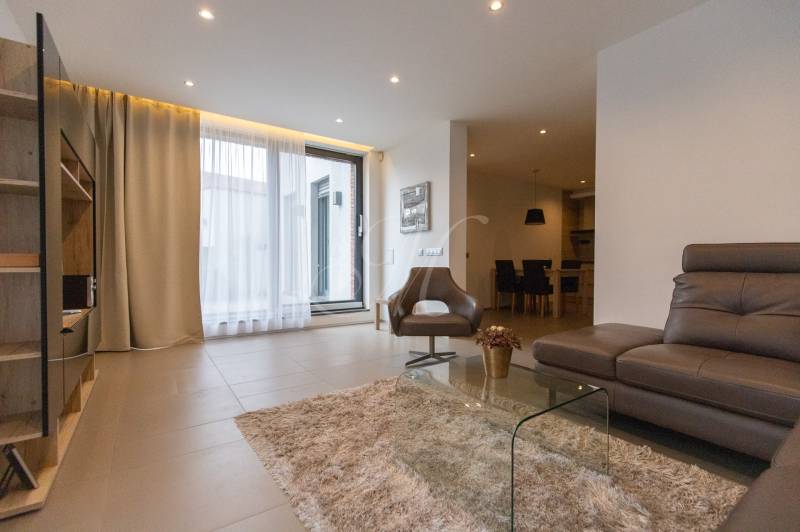 Nappali egy kétszobás lakásban kényelmes kanapéval, fotellel és üvegasztallal.