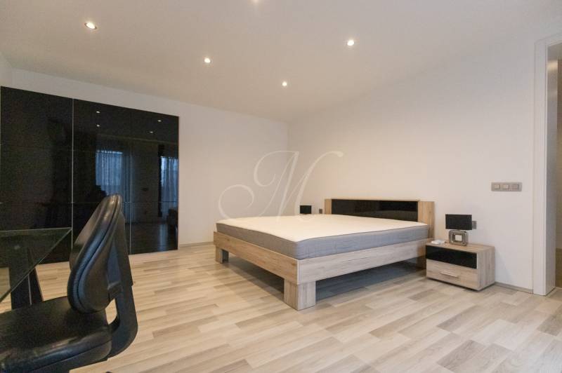 2 szobás lakás fa mintázatú padlóval, ággyal, szekrénnyel és irodai székkel.