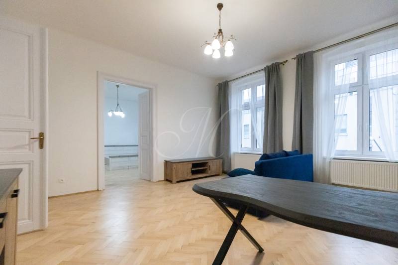 Nappali egy háromszobás lakásban, fa hatású padlóval és kék kanapéval.