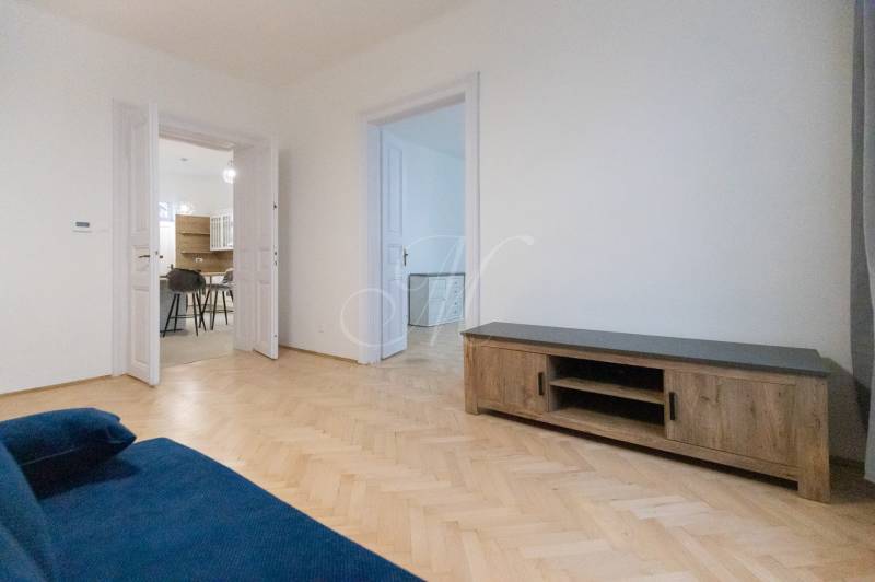 Háromszobás lakás nappalija kék kanapéval és fa dekorációjú padlóval.