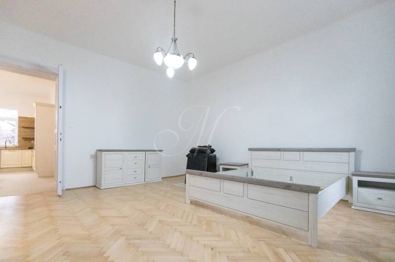 Hálószoba ággyal, bútorokkal és fa dekorációjú padlóval egy háromszobás lakásban.