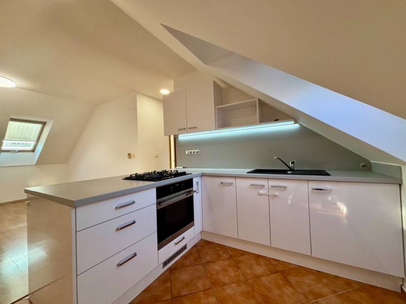 Világos konyha tetőtéri ablakkal, sarok munkalappal és kerámia padlóval egy kétszobás lakásban.