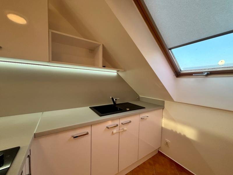 Konyha egy kétszobás lakásban fehér szekrényekkel és nagy tetőablakkal.