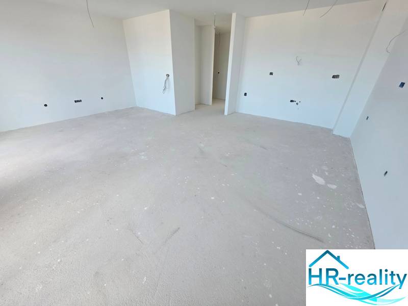 Tágas, befejezetlen szoba a Rekreációs apartmanban fehér falakkal és betonpadlóval.