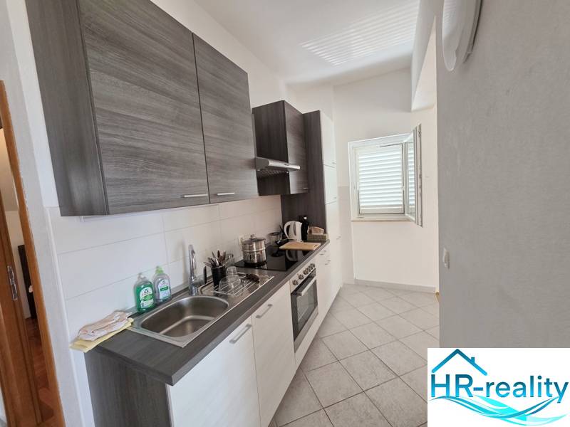 A modern felszereltségű és ablakkal rendelkező nyaraló apartman konyhája, amely megvilágítja a teret.