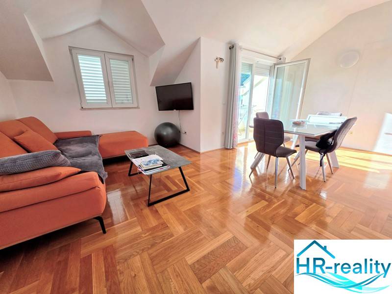 Nyaraló apartman narancssárga kanapéval, étkezőasztallal és fa dekorációjú padlóval.