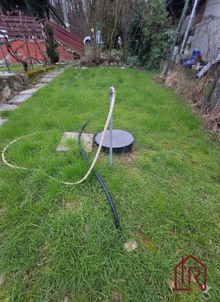 A hétvégi ház kertje Semsén, gyep kúttal és tömlővel.