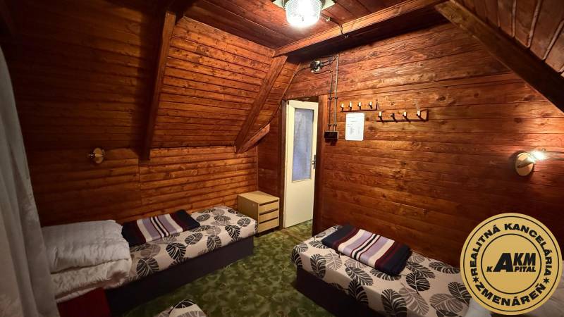 A faház belső tere fa burkolattal, ágyakkal és csillárral, otthonos környezet a pihenéshez.