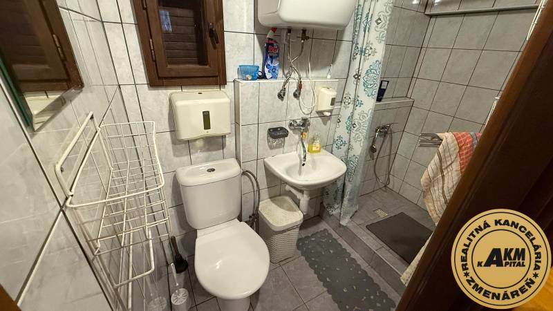 Fürdőszoba a házikóban zuhanyzóval, mosdóval, WC-vel és csempézett falakkal.