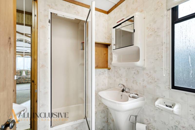 Fürdőszoba a házikóban mosdóval, zuhanyzóval és tükörrel, fa elemekkel.