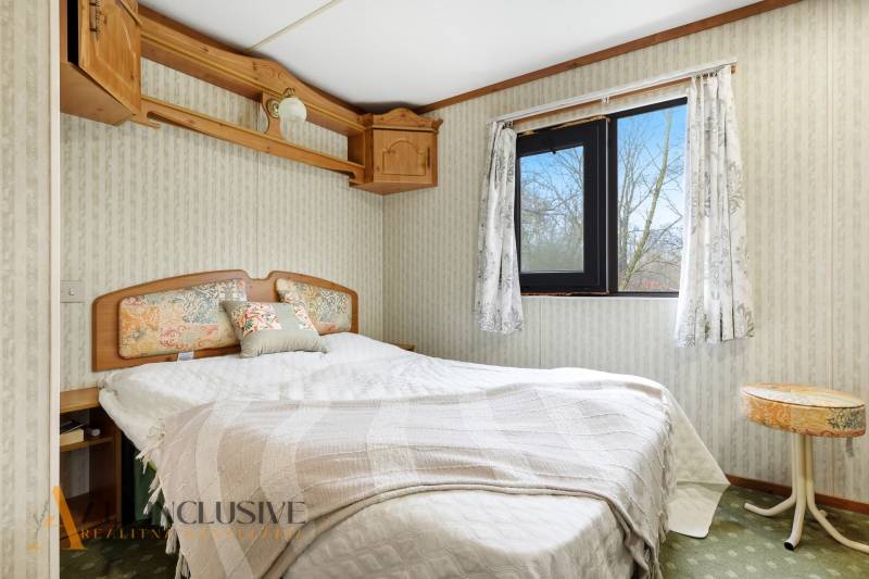 Hálószoba egy faházban virágos kiegészítőkkel, egy ablakkal és fa bútorokkal.