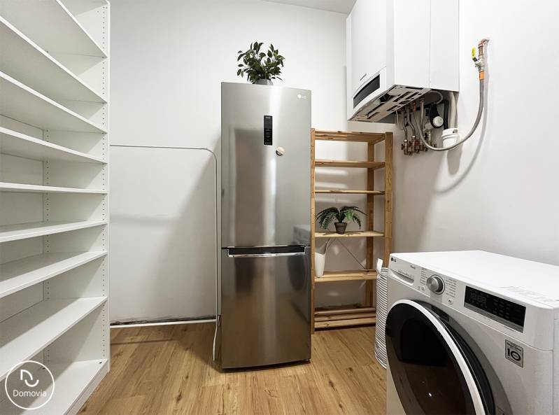 Hűtőszekrény és mosógép egy kétszobás lakásban a Vajnorská utcán, polcokkal és növényekkel kiegészítve.