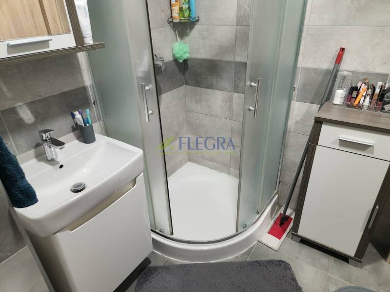 Fürdőszoba sarokzuhannyal, mosdóval és szekrénnyel egy kétszobás lakásban.