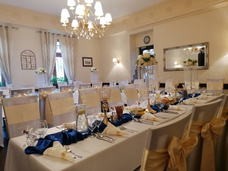 Esküvői dekoráció a szállodai étterem belső terében, elegánsan megterített asztalok virágdíszítéssel.