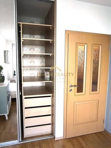 Nyitott szekrény polcokkal és fiókokkal egy kétszobás lakásban, fa dekoros padlóval.