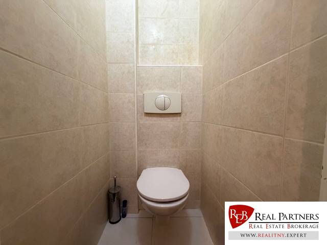 Fehér csempével burkolt és beépített WC-vel rendelkező toalett egy háromszobás lakásban.