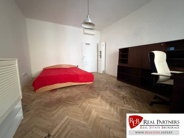 Szoba ággyal, íróasztallal és fa dekorációjú padlóval egy háromszobás lakásban.