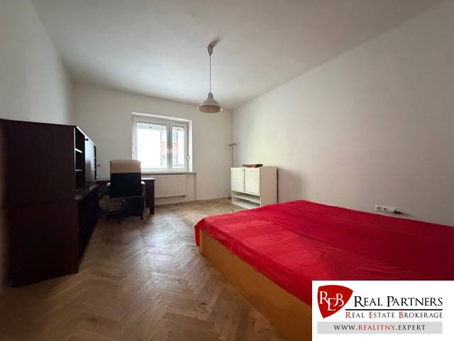 Hálószoba egy háromszobás lakásban, ággyal, íróasztallal és fa dekorációjú padlóval.