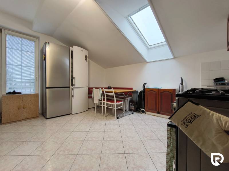 Családi ház konyhája ferde mennyezettel, nagy hűtőszekrénnyel és étkezőasztallal.