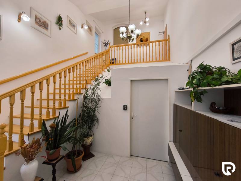 Egy családi ház belső terében található egy fa lépcső, növények és világítótestek.