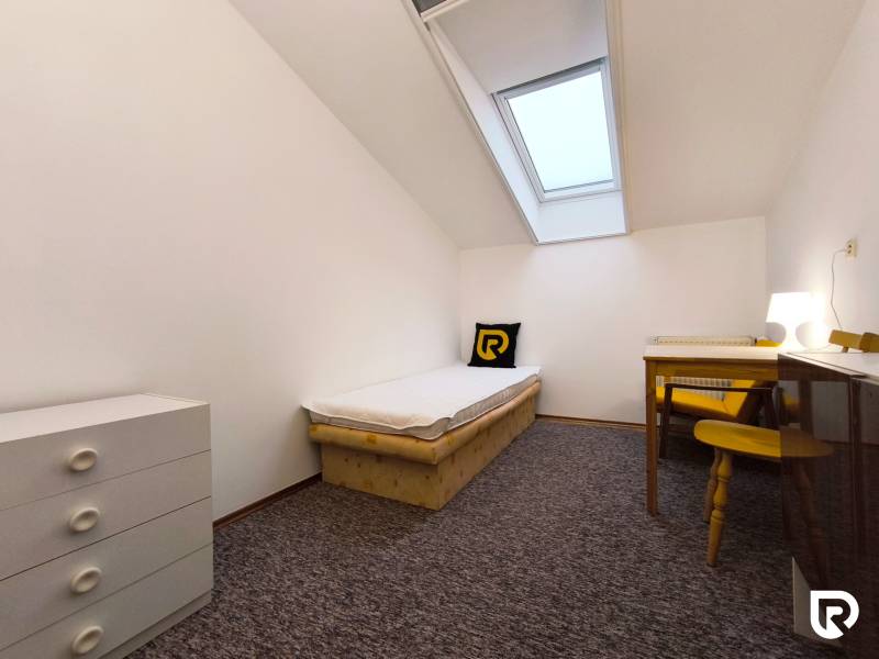 Egyszerű szoba egy ággyal, asztallal és komóddal egy családi házban.