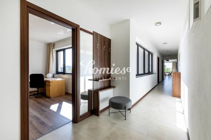 Világos folyosó dolgozószobával és fa dekoros padlóval egy háromszobás lakásban.